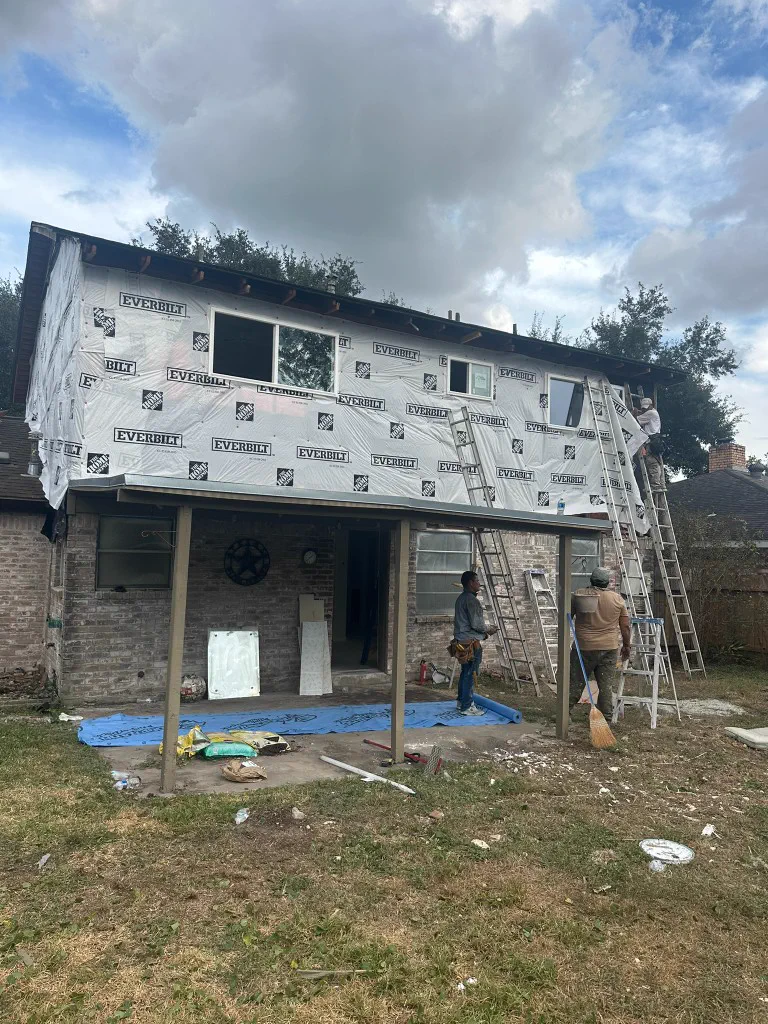 Crew on ladders during exterior siding and wrap work on a two-story home