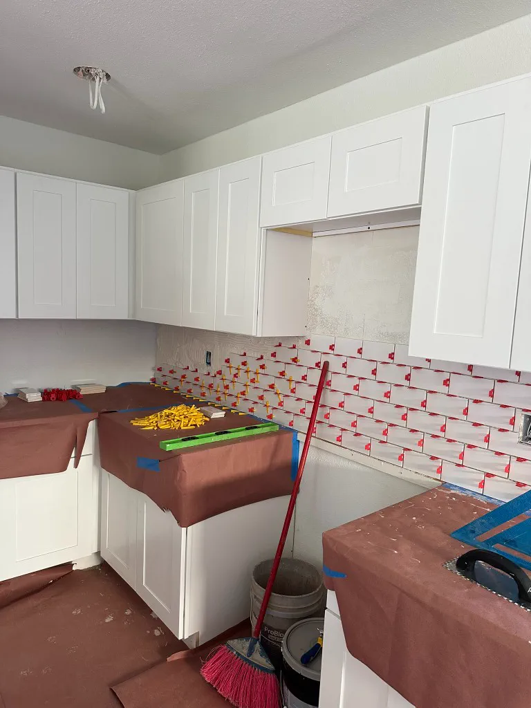 Subway tile backsplash in progress with spacers and leveling tools on the counter